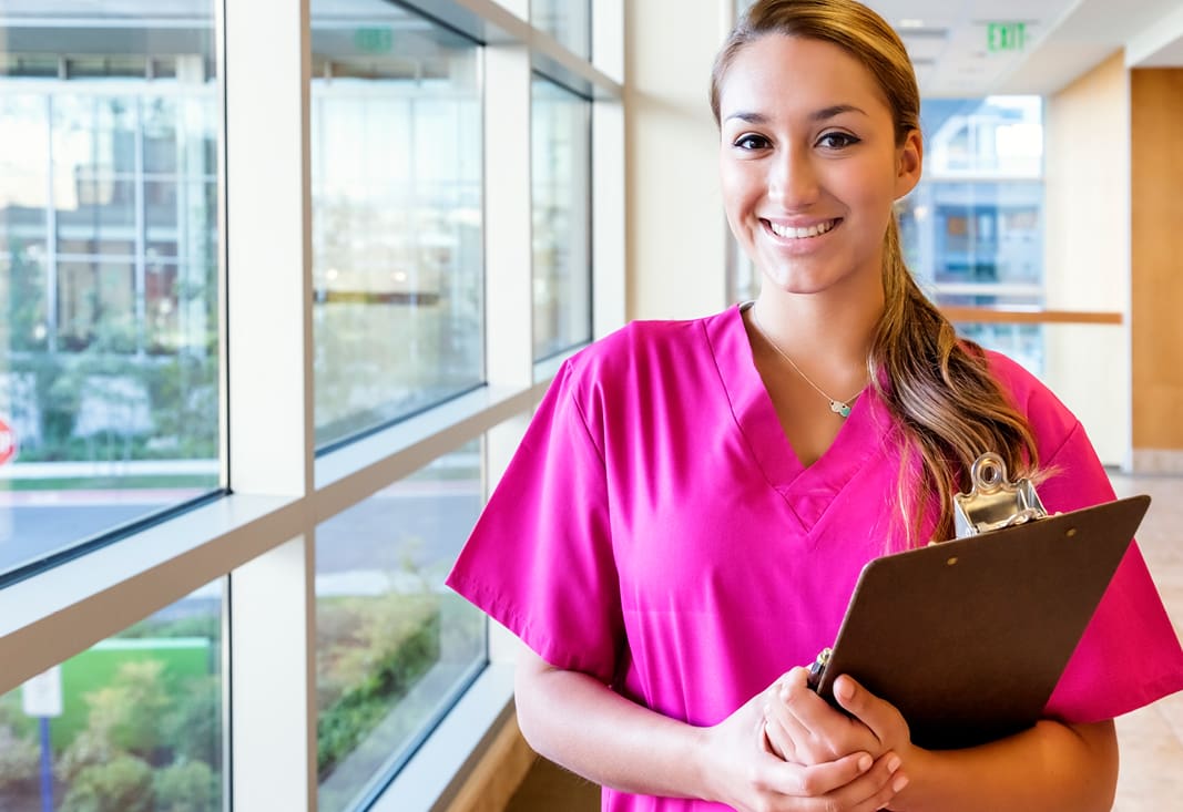 healthcare worker in pink scrubs holding a clipboard.